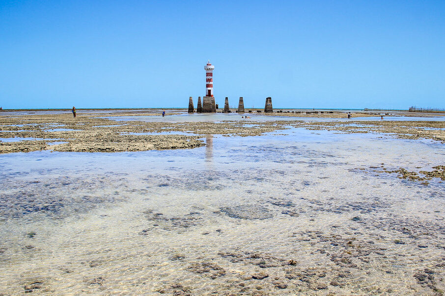 Vista do farol de Maceió ao longe em uma maré baixa próximo os bairros de Pajuçara, Ponta Verde, Jatiúca e Cruz das Almas.